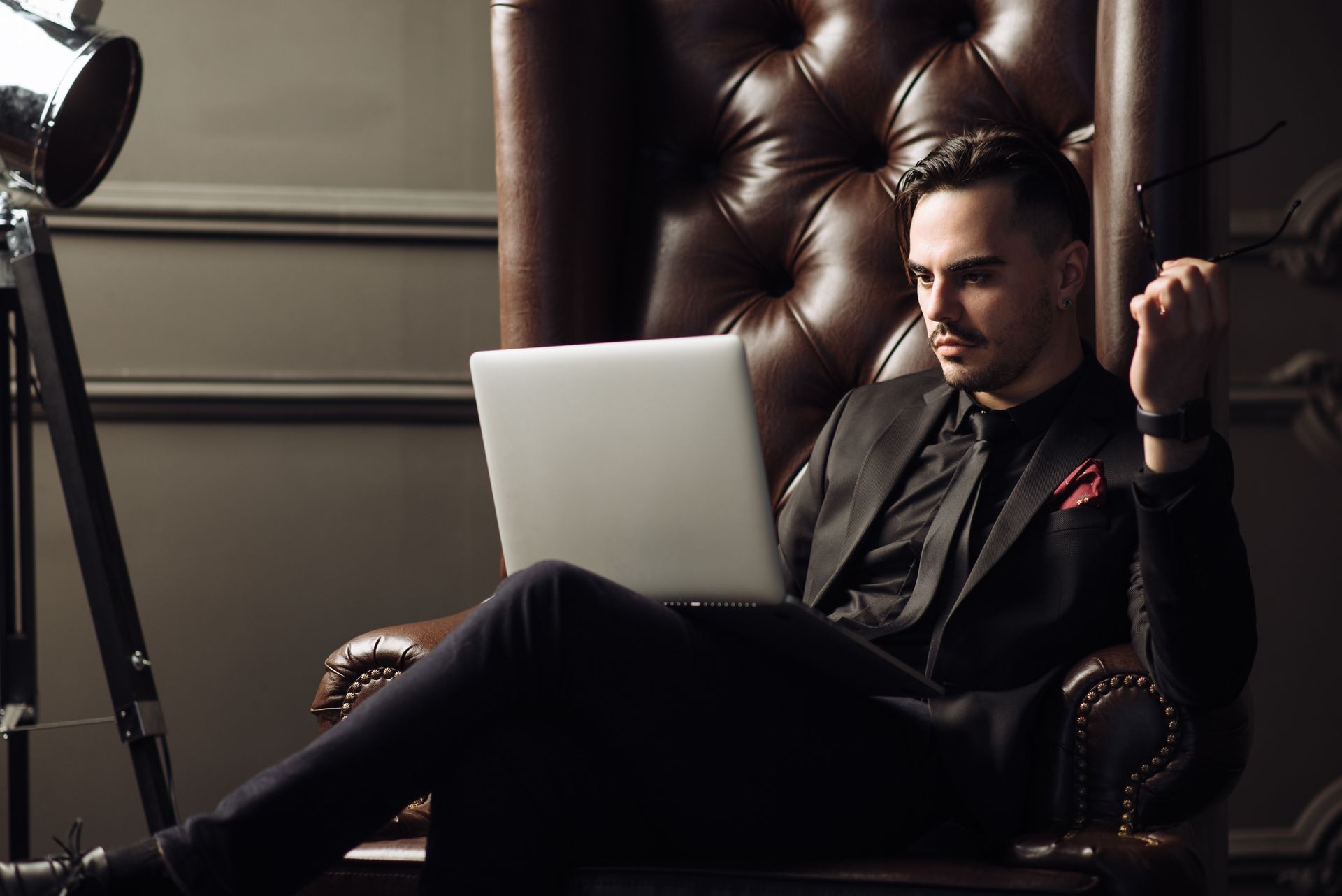 Young handsome successful boss sitting in a leather armchair in luxury fashionable interior thinking about his plans of future development of his worldwide well-known digital marketing company. 